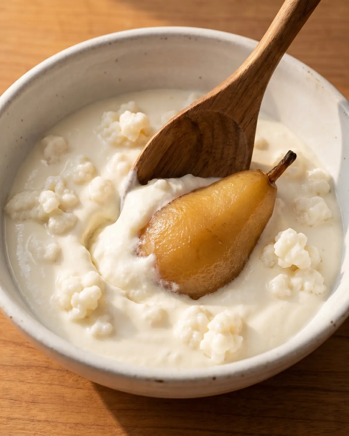 Cucchiaio di legno che lascia un solco nel kefir cremoso con pera cotta in una ciotola bianca.