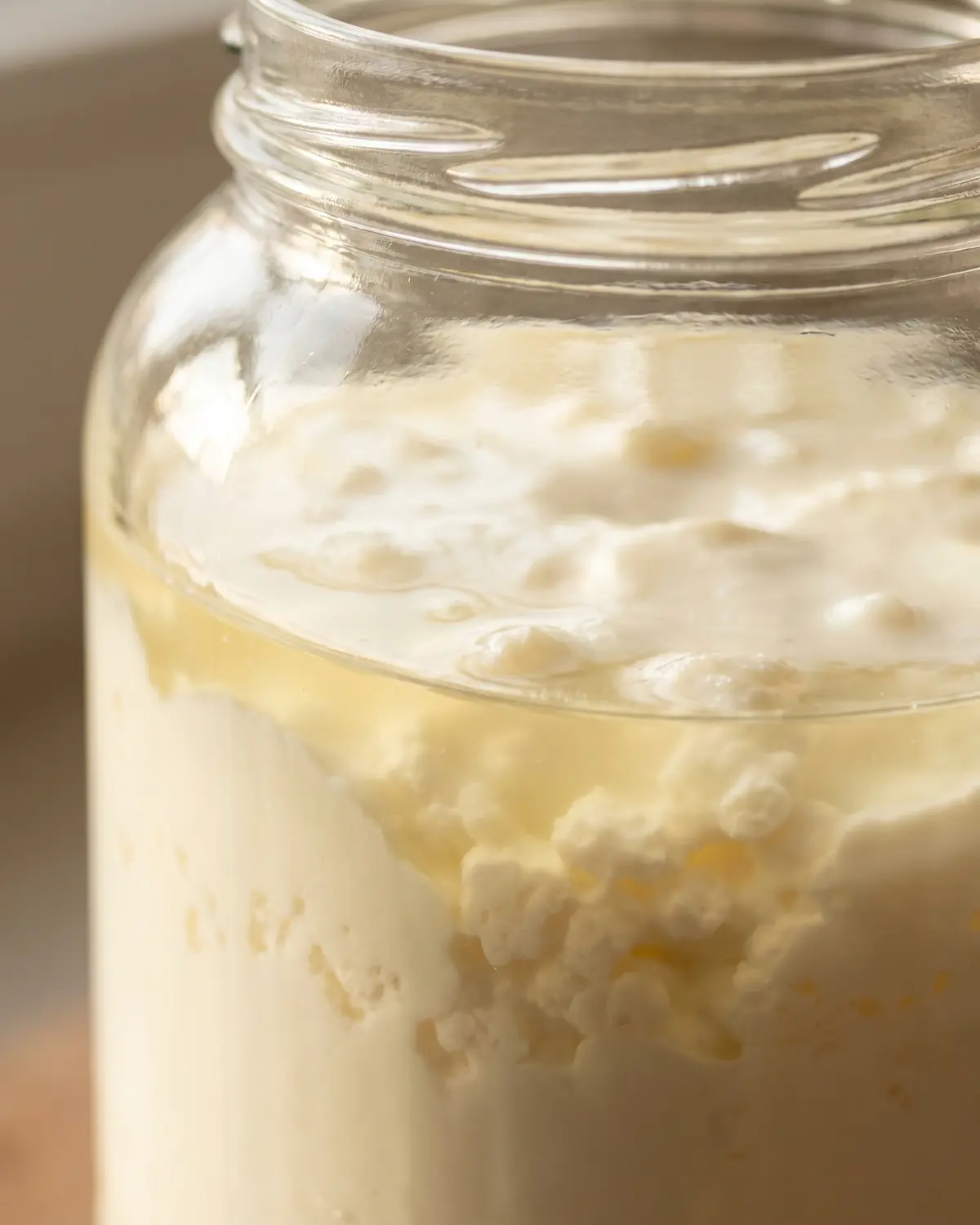 Primo piano di un barattolo di kefir con la separazione visibile tra siero e parte cremosa.