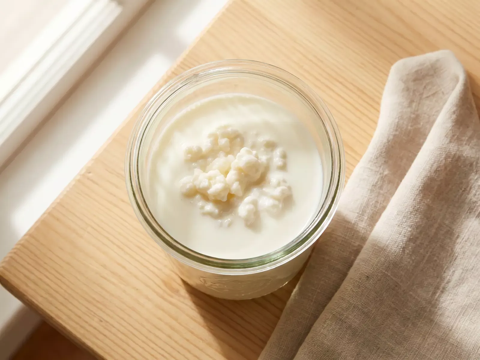 Vista dall&rsquo;alto di un barattolo di kefir di latte in fermentazione su legno con panno di lino.