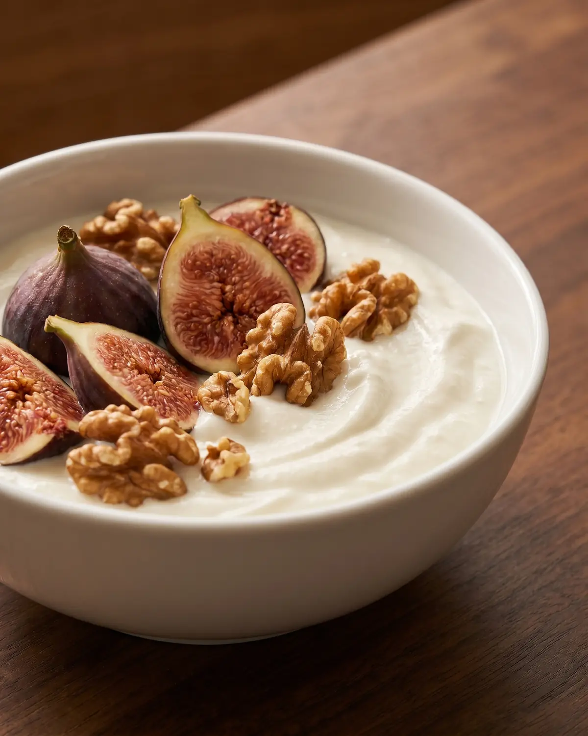 yogurt greco Yogurt servito in una ciotola bianca con fichi freschi e noci su un piano in legno scuro.