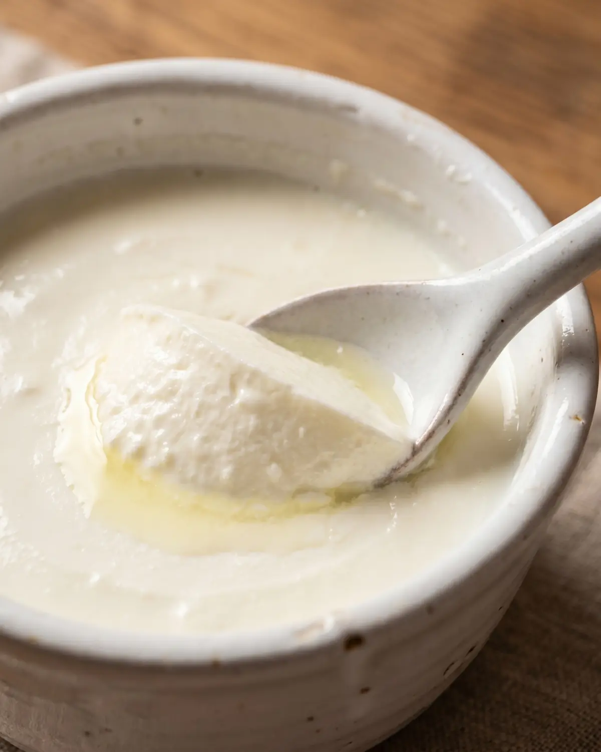 Primo piano di yogurt compatto separato con cucchiaio, con taglio netto e lieve siero brillante.